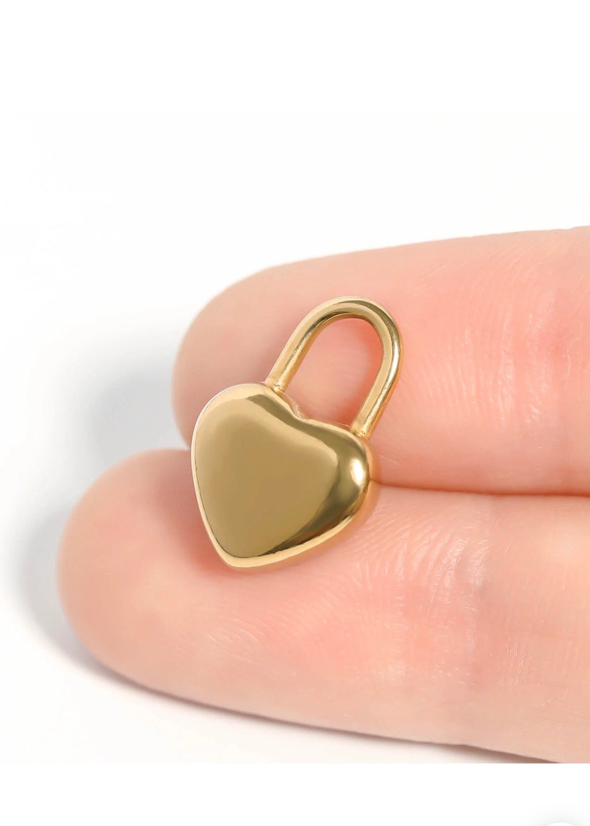 Gold heart lock charm held between fingers showing scale