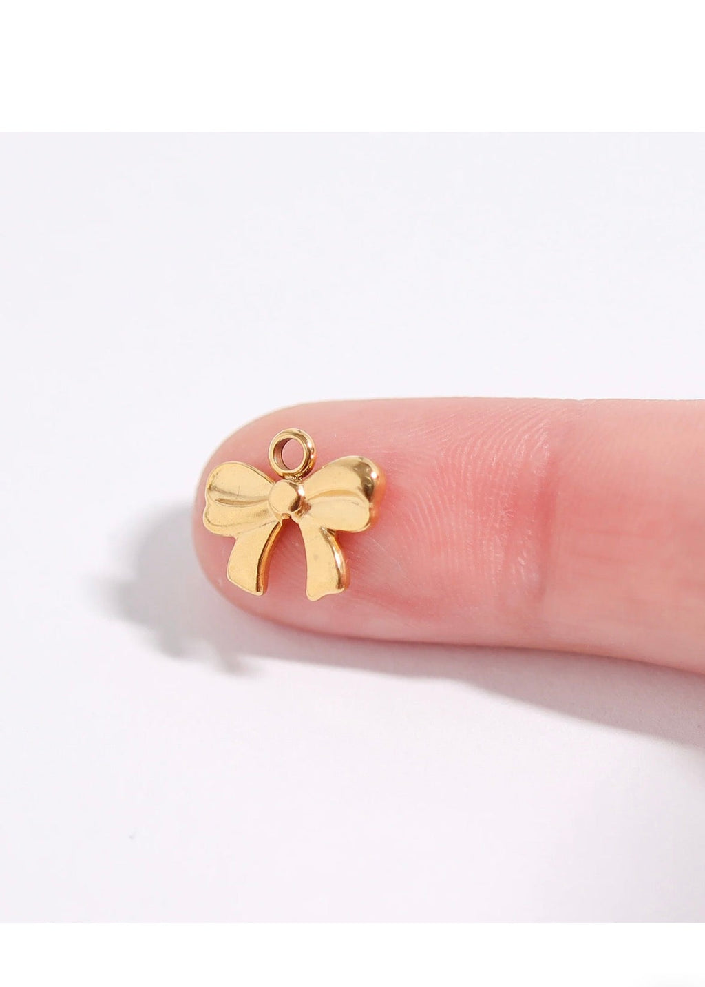 A small gold bow-shaped charm resting on a person's fingertip against a plain white background.