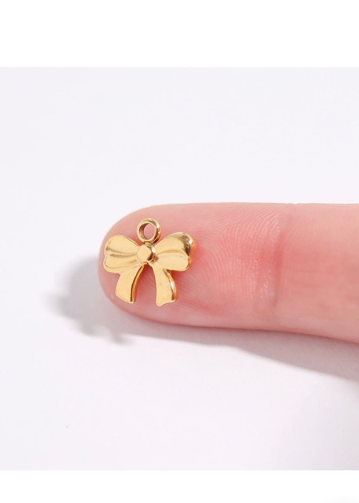 A small gold bow-shaped charm resting on a person's fingertip against a plain white background.